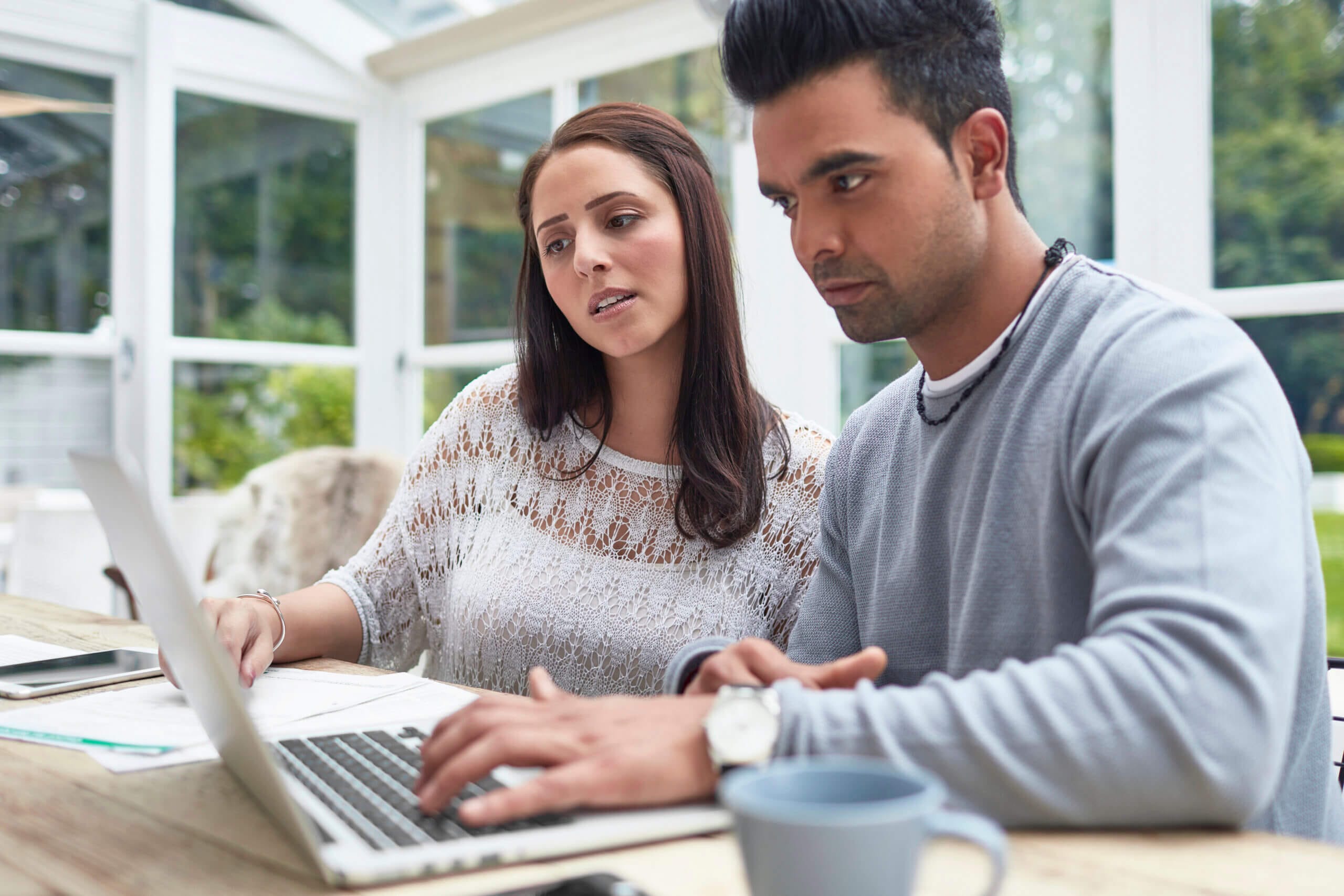 younger couple sat at a table looking at a laptop